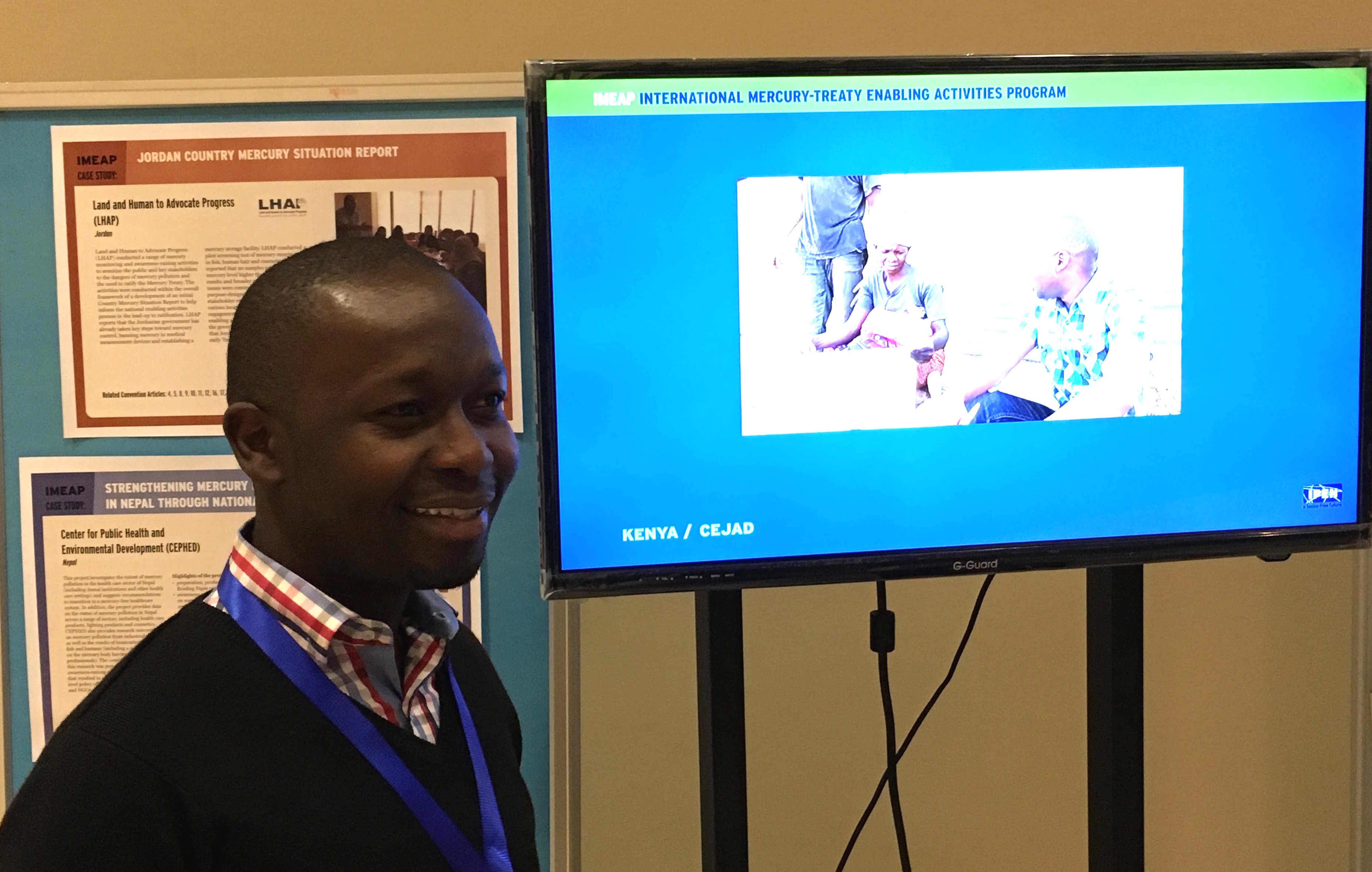 Griffins Ochieng (CEJAD) standing near the ASGM-related video that CEJAD produced for their IMEAP project with IPEN